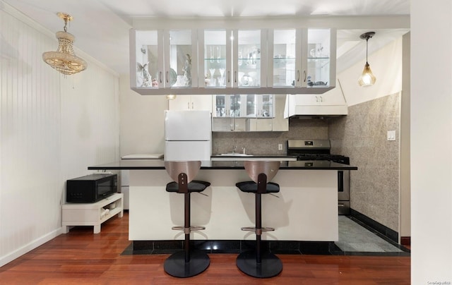 kitchen featuring a breakfast bar, white refrigerator, hanging light fixtures, stainless steel gas stove, and dark hardwood / wood-style flooring