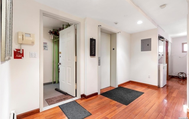 hallway featuring elevator, wood-type flooring, electric panel, and a baseboard heating unit