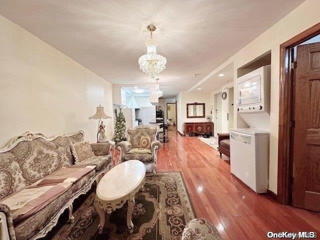 living room with hardwood / wood-style flooring, a chandelier, and stacked washer and clothes dryer