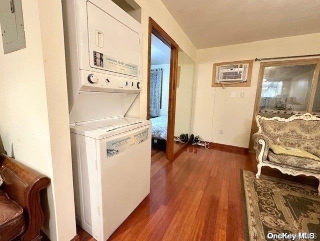 laundry room with electric panel, dark wood-type flooring, a wall unit AC, and stacked washer and clothes dryer