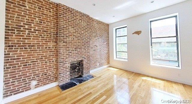 unfurnished living room with a fireplace, brick wall, and hardwood / wood-style flooring