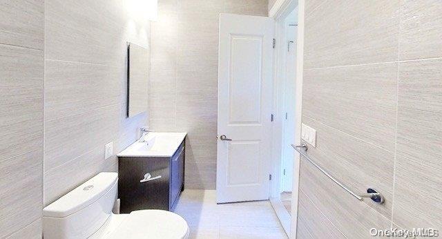 bathroom featuring tile patterned flooring, vanity, tile walls, and toilet