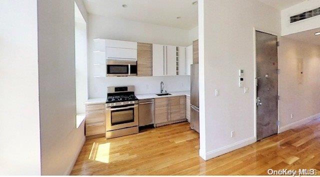 kitchen with white cabinets, appliances with stainless steel finishes, light hardwood / wood-style flooring, and sink