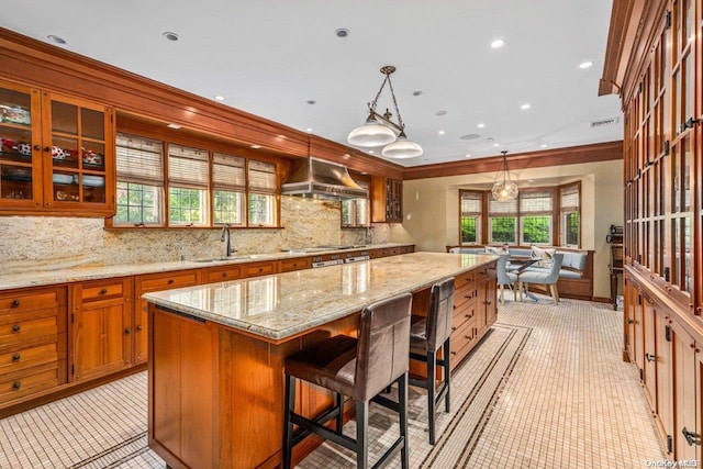 kitchen with a large island, sink, hanging light fixtures, wall chimney range hood, and crown molding