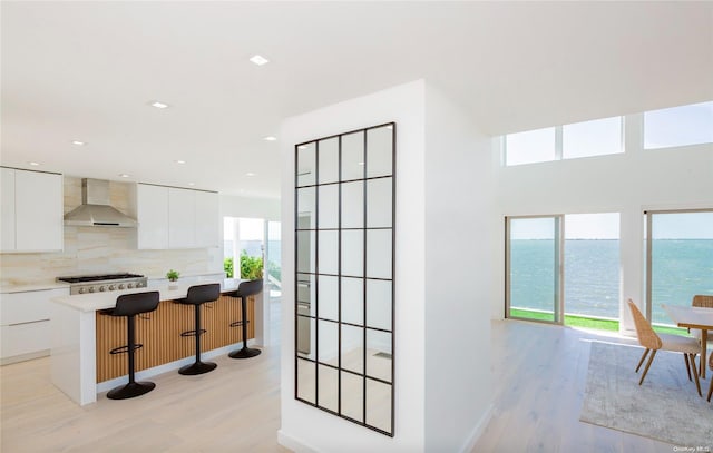 kitchen with white cabinetry, wall chimney exhaust hood, a kitchen island, light hardwood / wood-style floors, and a water view