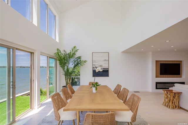 dining room with a towering ceiling, a water view, a healthy amount of sunlight, and light hardwood / wood-style floors