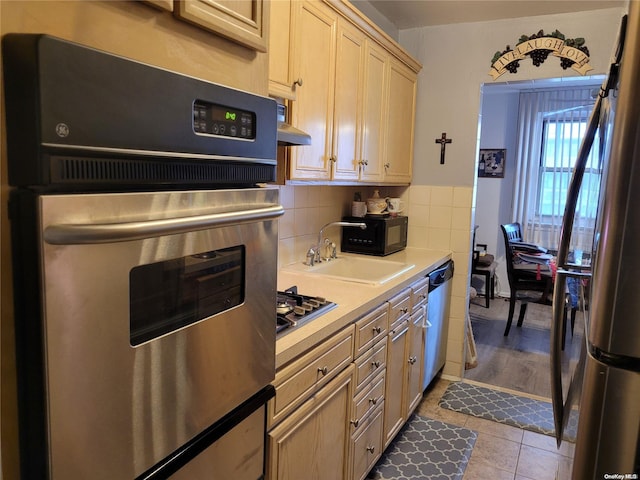 kitchen featuring decorative backsplash, light tile patterned floors, range hood, light brown cabinetry, and stainless steel appliances