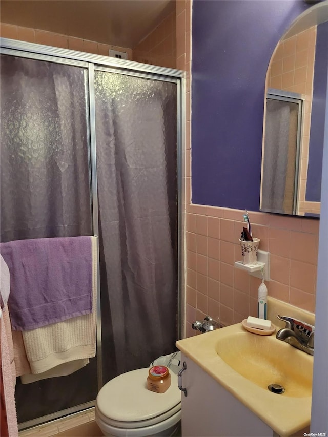 bathroom featuring vanity, toilet, a shower with shower door, and tile walls