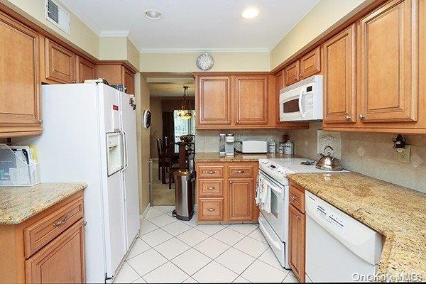 kitchen with light stone counters, white appliances, backsplash, and ornamental molding