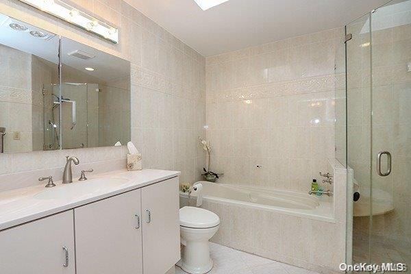 full bathroom with vanity, tile patterned floors, toilet, shower with separate bathtub, and tile walls