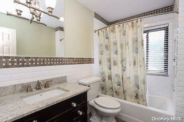 full bathroom with vanity, shower / bath combination with curtain, tile walls, and toilet