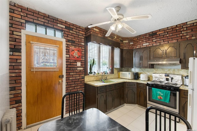 kitchen with white appliances, radiator, sink, dark brown cabinets, and brick wall