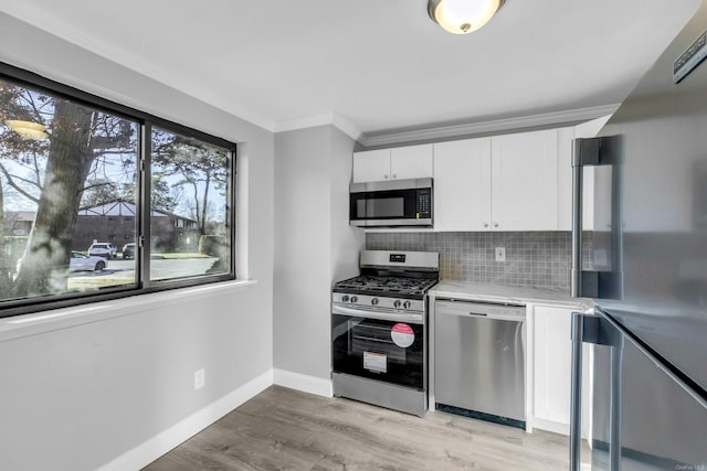 kitchen with tasteful backsplash, white cabinetry, ornamental molding, light hardwood / wood-style floors, and stainless steel appliances