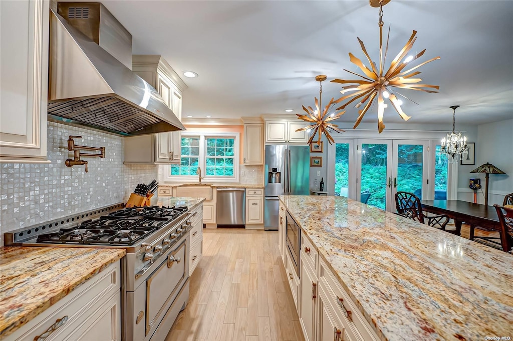 27 Prospect Ave, Sea Cliff, NY 11579 - kitchen with hanging light fixtures, wall chimney exhaust hood, light stone countertops, appliances with stainless steel finishes, and a notable chandelier