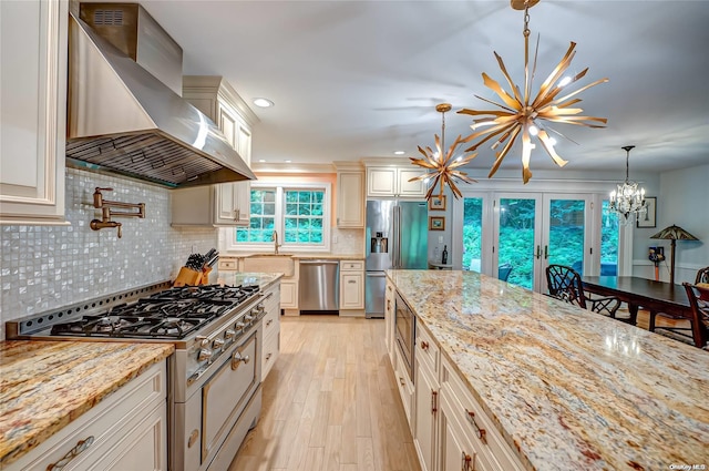 27 Prospect Ave, Sea Cliff, NY 11579 - kitchen with hanging light fixtures, wall chimney exhaust hood, light stone countertops, appliances with stainless steel finishes, and a notable chandelier