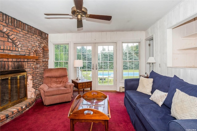 living room with carpet flooring, ceiling fan, french doors, a brick fireplace, and wooden walls