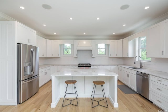 kitchen with stainless steel appliances, sink, a center island, light hardwood / wood-style floors, and white cabinetry