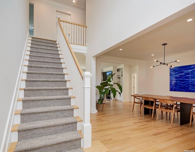 staircase featuring hardwood / wood-style floors, crown molding, and a notable chandelier