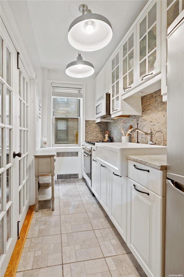 kitchen with decorative backsplash, light stone countertops, radiator, stainless steel appliances, and white cabinets