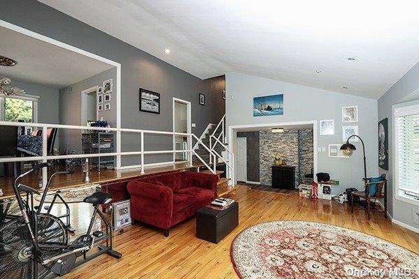 living room featuring a stone fireplace, lofted ceiling, wood-type flooring, and plenty of natural light