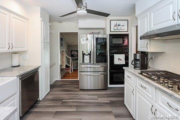 kitchen with backsplash, white cabinets, wall chimney range hood, and black appliances