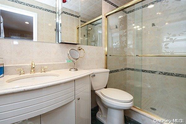 bathroom with tile walls, toilet, vanity, and a shower with shower door