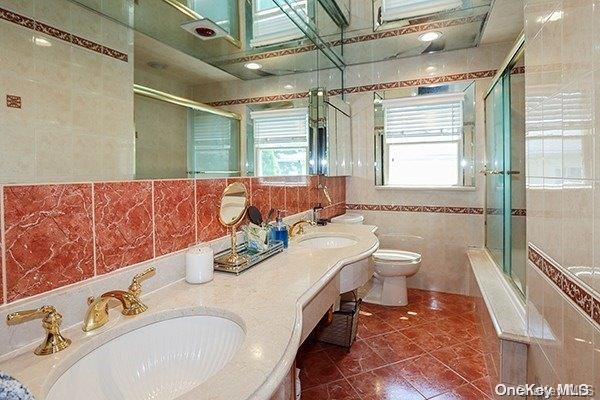 full bathroom with toilet, tile walls, a healthy amount of sunlight, and bath / shower combo with glass door