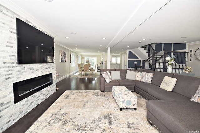 living room with crown molding, dark wood-type flooring, and a stone fireplace