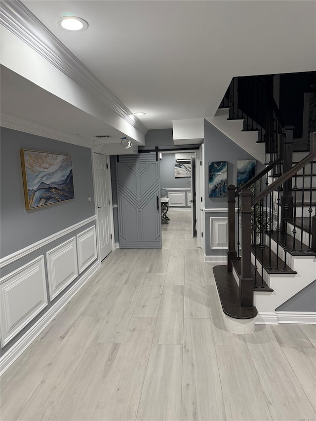 interior space with light hardwood / wood-style floors, crown molding, and a barn door