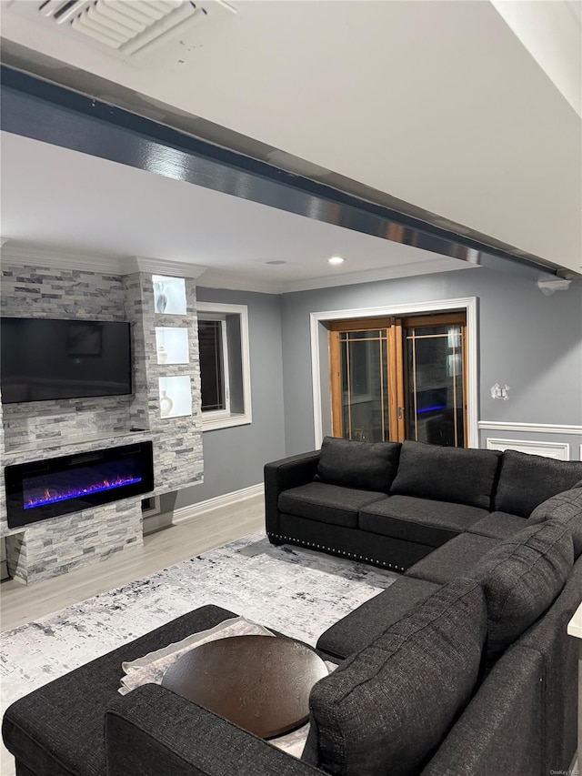 living room featuring wood-type flooring, ornamental molding, and a stone fireplace