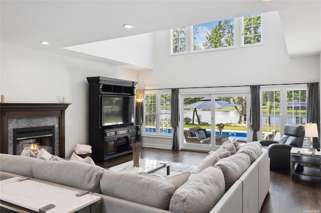 living room with a fireplace, a towering ceiling, a wealth of natural light, and dark wood-type flooring