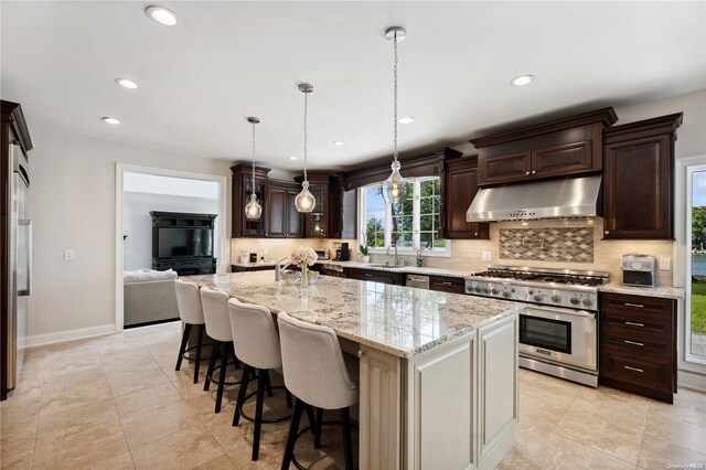 kitchen featuring backsplash, light stone counters, stainless steel appliances, hanging light fixtures, and an island with sink