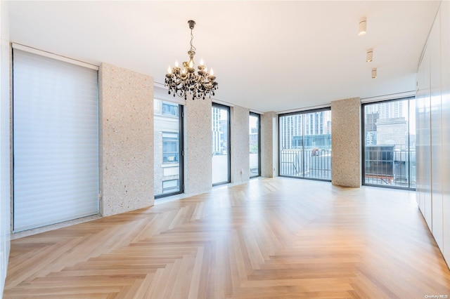 unfurnished room featuring expansive windows, light parquet flooring, a healthy amount of sunlight, and a notable chandelier