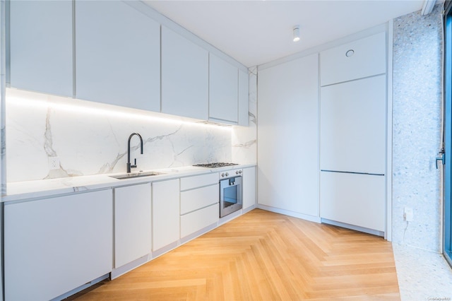 kitchen with light stone countertops, sink, stainless steel appliances, light parquet floors, and white cabinets