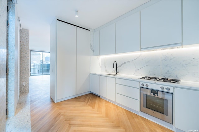 kitchen with light stone countertops, sink, light parquet floors, white cabinets, and appliances with stainless steel finishes