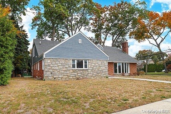 127 Berkshire Rd, Rockville Centre, NY 11570 - view of front of home featuring a chimney, stone siding, and a front lawn