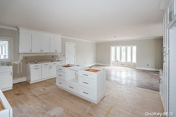 127 Berkshire Rd, Rockville Centre, NY 11570 - kitchen with crown molding, light wood finished floors, white cabinets, a center island, and open floor plan
