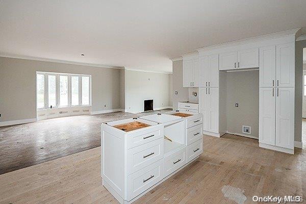 127 Berkshire Rd, Rockville Centre, NY 11570 - kitchen with ornamental molding, light wood-type flooring, white cabinetry, a center island, and open floor plan