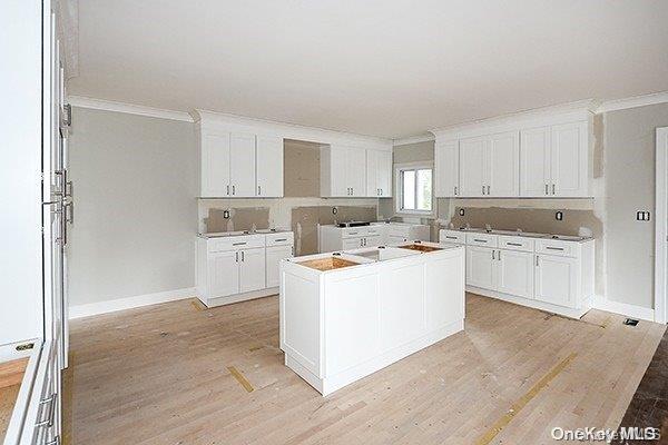 kitchen with white cabinetry, crown molding, and light hardwood / wood-style flooring