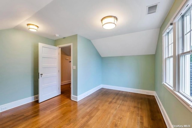 additional living space with light hardwood / wood-style flooring, a healthy amount of sunlight, and vaulted ceiling