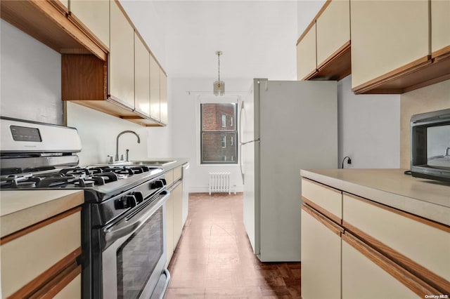 kitchen with gas range, sink, radiator heating unit, white fridge, and cream cabinetry