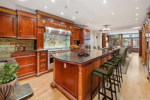 kitchen featuring dark stone counters, light hardwood / wood-style flooring, high quality appliances, and an island with sink