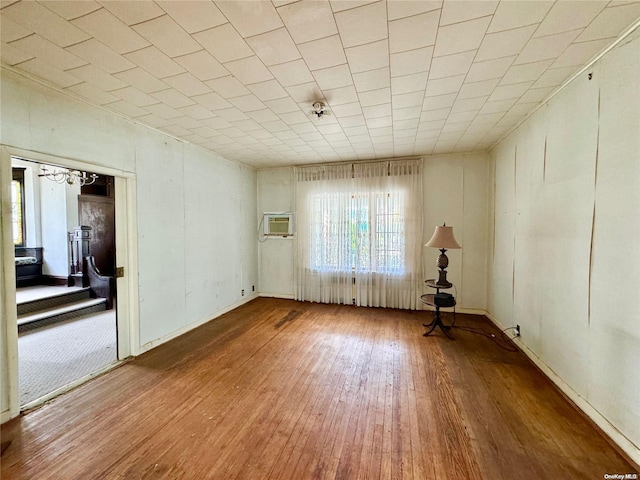 spare room featuring a chandelier, a wall mounted air conditioner, and hardwood / wood-style flooring