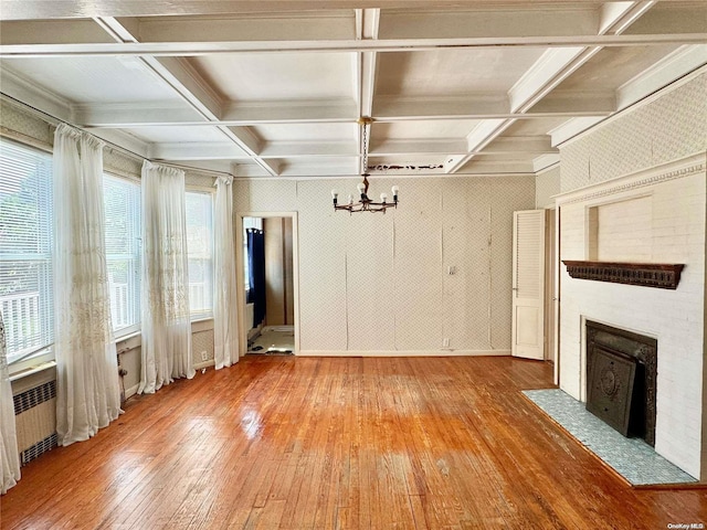 unfurnished living room featuring a chandelier, a healthy amount of sunlight, wood-type flooring, and coffered ceiling