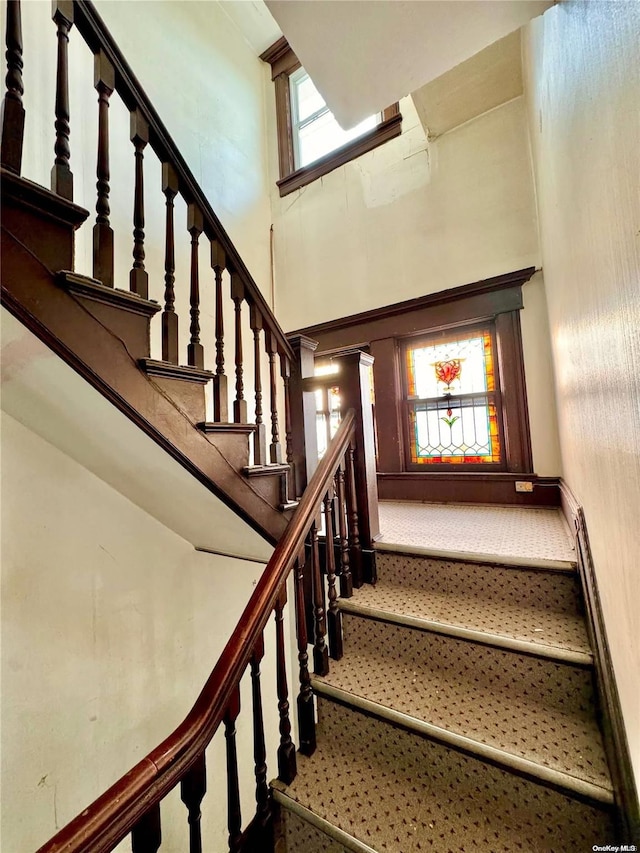 stairs with plenty of natural light, a towering ceiling, and a baseboard heating unit