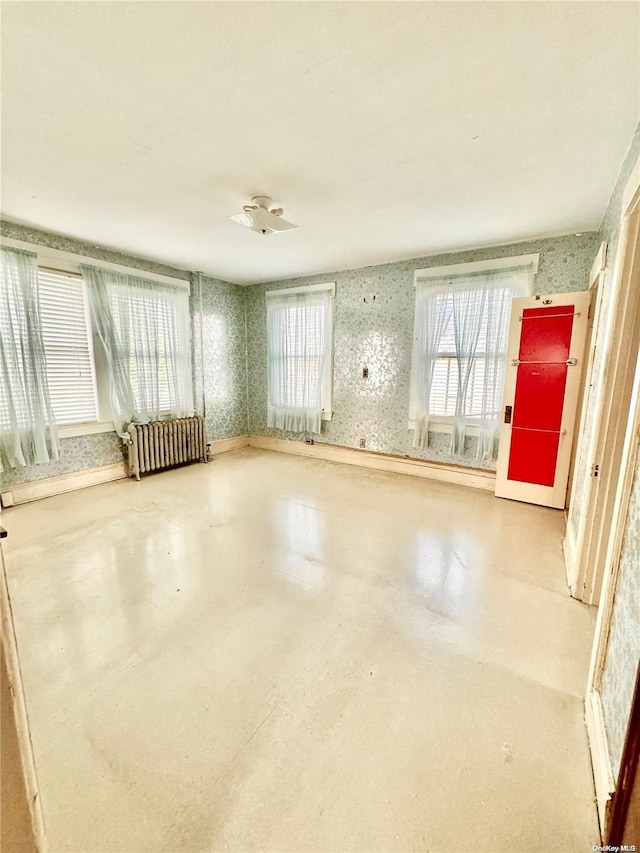 unfurnished room featuring a wealth of natural light, radiator heating unit, and concrete floors