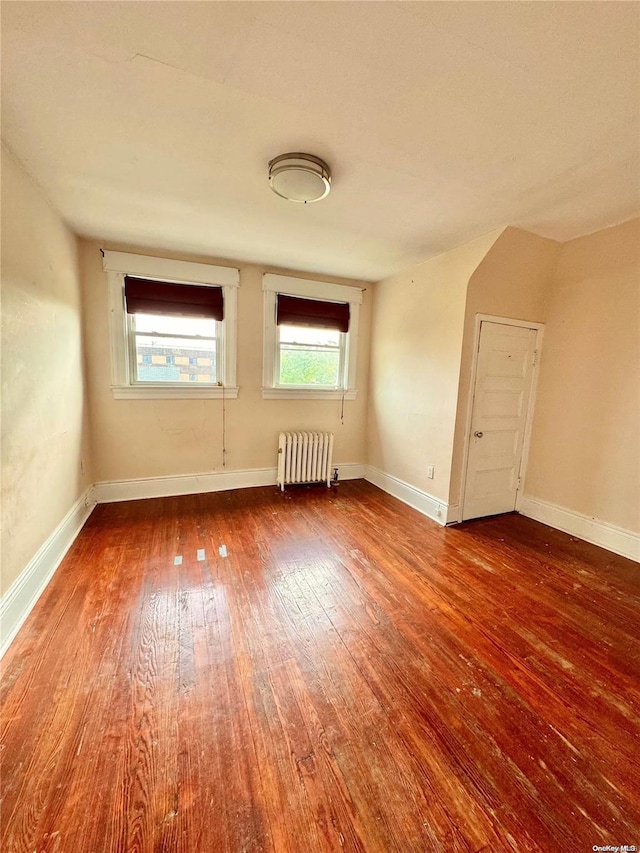 empty room with a wealth of natural light, radiator, and wood-type flooring