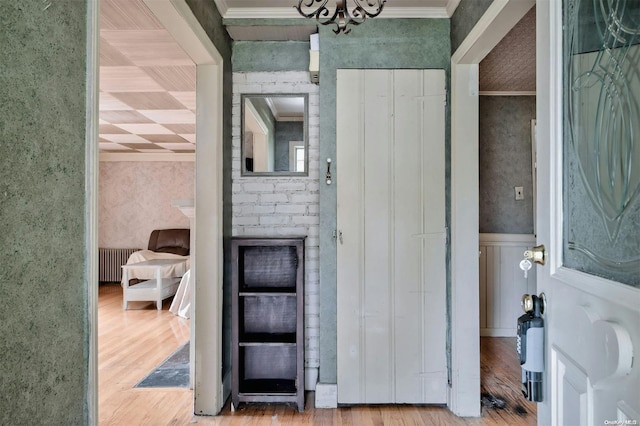 hall with a chandelier, wood-type flooring, radiator heating unit, and crown molding