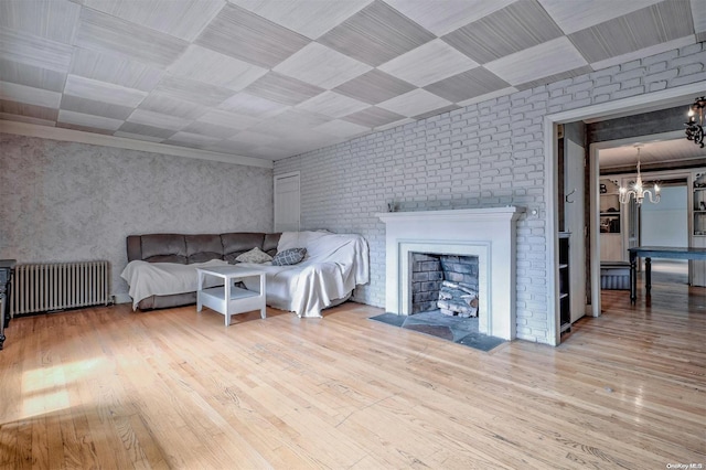 bedroom with radiator, an inviting chandelier, a brick fireplace, light hardwood / wood-style flooring, and brick wall