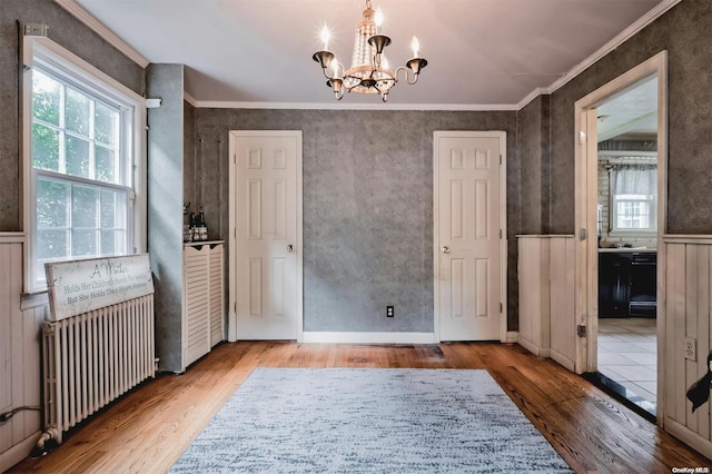 interior space featuring wood-type flooring, ornamental molding, radiator, and an inviting chandelier